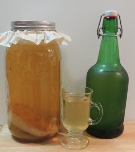 2 qt. jar of kombucha fermenting next to bottle and glass with finished product