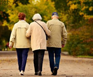 Backs of three elderly people walking arm-in arm down a road 