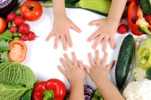 children's hands on cutting board with vegetables