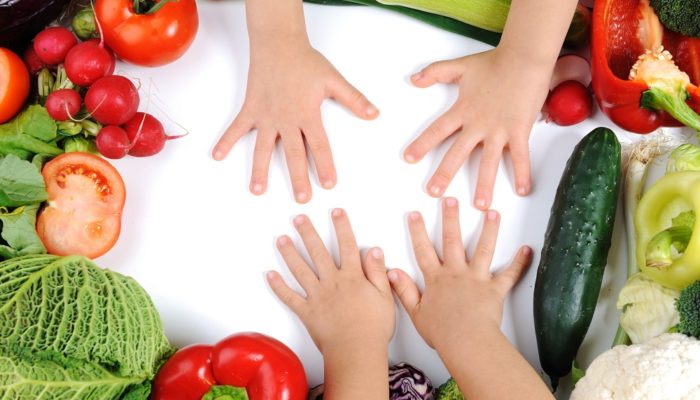 children's hands on cutting board with vegetables