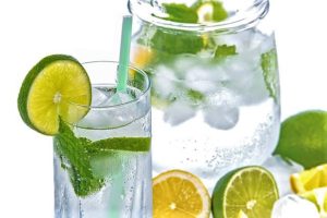 Glass and pitcher of cold water with slices of lemons and limes