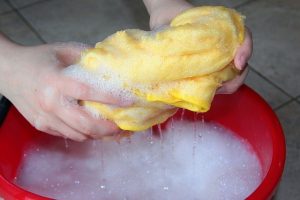 wringing cloth out over soapy bucket of water