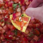 persons hand dipping into tomato salsa