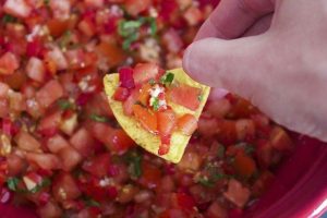 persons hand dipping into tomato salsa