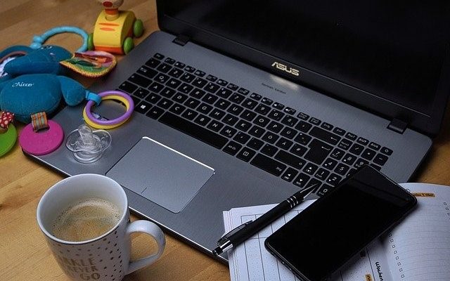 Photo contains a laptop, cellphone, calendar, pen, hot beverage, and children's toys.