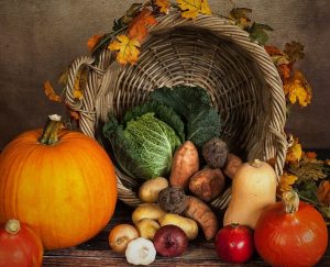 pumpkin and fall vegetables in front of a fall leaf decorated basket