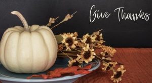 white pumpkin and fall flowers on a table that says "Give Thanks"