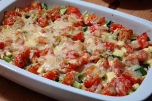 Casserole dish containing zucchini, noodles , tomatoes and cheese