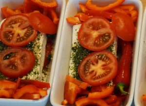 Two casserole dishes filled with red bell peppers, tomatoes, cheese and herbs