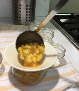 ladeling peach preserves into a jar for canning