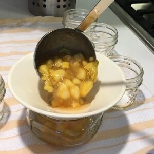 ladeling peach preserves into a jar for canning