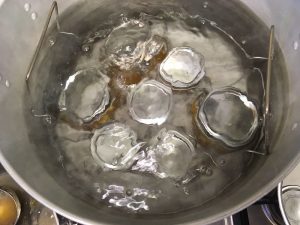 Peach preserves jars are placed into a waterbath canner and covered by 1 inch of water to bring to a boil and begin processing.