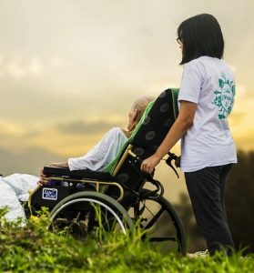 Woman caring for an elderly patient in a wheelchair. Both are outside watching the sun set