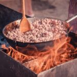cooking ground meat in a deep pan over flames