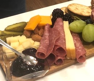 Jam, cheese cubes, rolled salami, and grapes on a board