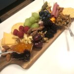 Cutting board topped with Jams, sliced cheese, nuts raspberries, grapes and rolled meat slices.