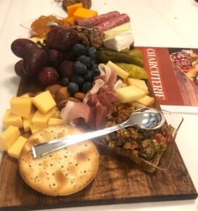 crackers, cheese cubes, nuts pickles and grapes on a board.