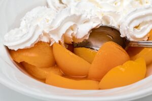 Bowl of canned peaches topped with whipped cream.