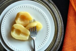 Three canned pears halves on a plate with a fork.