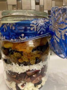 Layers in dried fruits and nuts in a clear jar, tied up with a festive blue and silver ribbon.