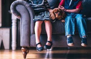 two children sitting on a couch with a dog in between them