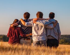 Four teens standing in a field, arms wrapped around each others shoulders, with their backs to the camera.