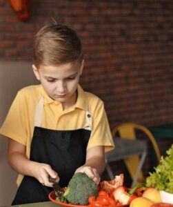 Young boy with apron on chopping vegetables