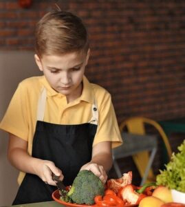 Young boy with apron on chopping vegetables