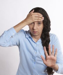 Woman with one hand on her forehead and another out in front of her as to say stop/enough.