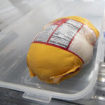 Thawing a chicken in its original packaging in a container at the bottom of the refrigerator