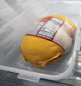 Thawing a chicken in its original packaging in a container at the bottom of the refrigerator