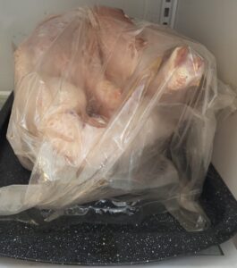 A fresh turkey in its bag on a tray thawing on the bottom shelf of the fridge