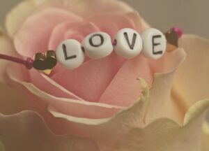 Beaded bracelet with letter beads spelling out the word "LOVE" on top of a light pink rose flower.