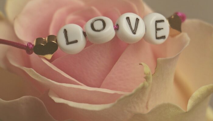 Beaded bracelet with letter beads spelling out the word "LOVE" on top of a light pink rose flower.