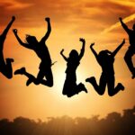 silhouette of five people jumping for joy in front of a sunrise