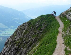 Outline of a person at the top of a steep path that overlooks a valley and mountains
